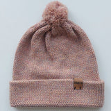 Handmade light pink baby hat in soft 100% baby alpaca wool with a pompom, foldable edge, and brown vegan leather label, offering warmth and comfort.