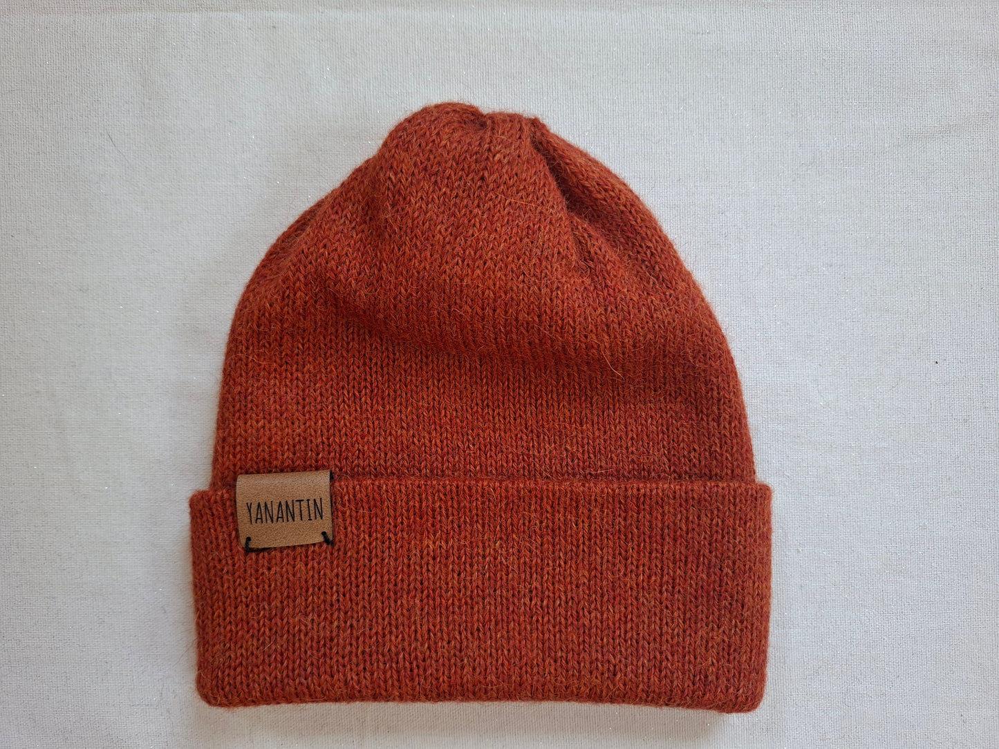 Orange alpaca wool knit beanie with a visible brand label on a light gray background
