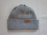 Gray knit beanie with a brown leather label on a light surface