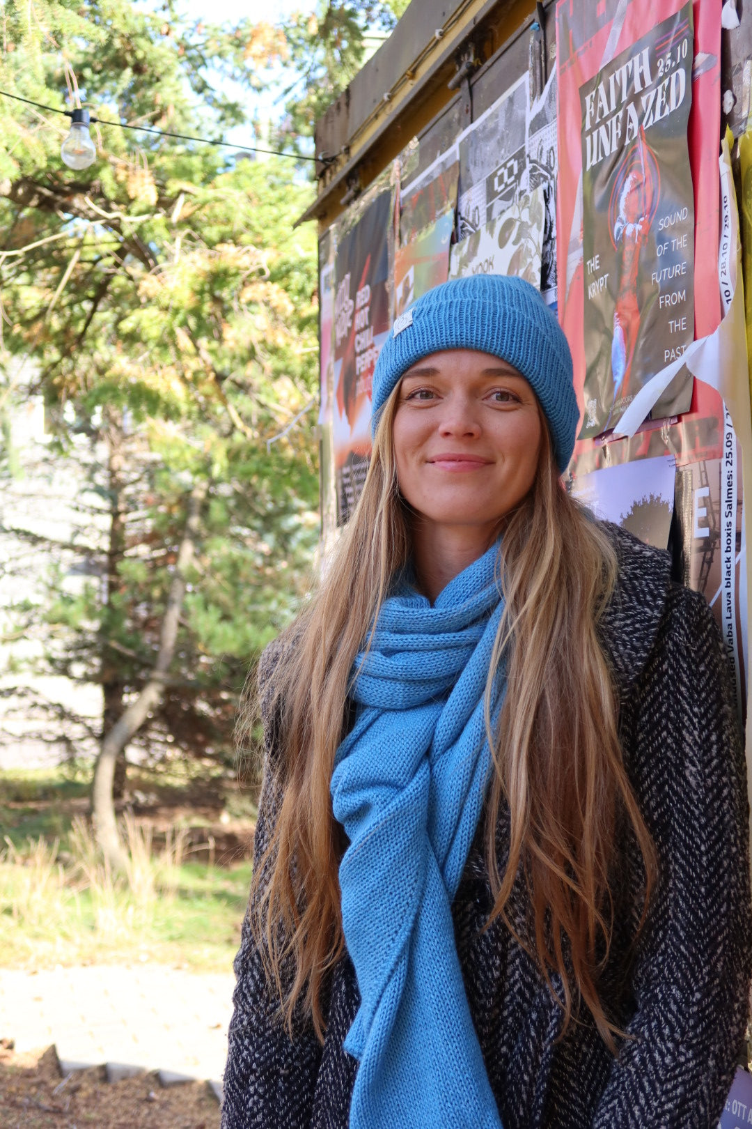 Young woman wearing a blue knit hat and scarf standing outdoors.