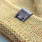 Close-up of the brown vegan leather label on the handmade light yellow baby hat, highlighting the quality and style.