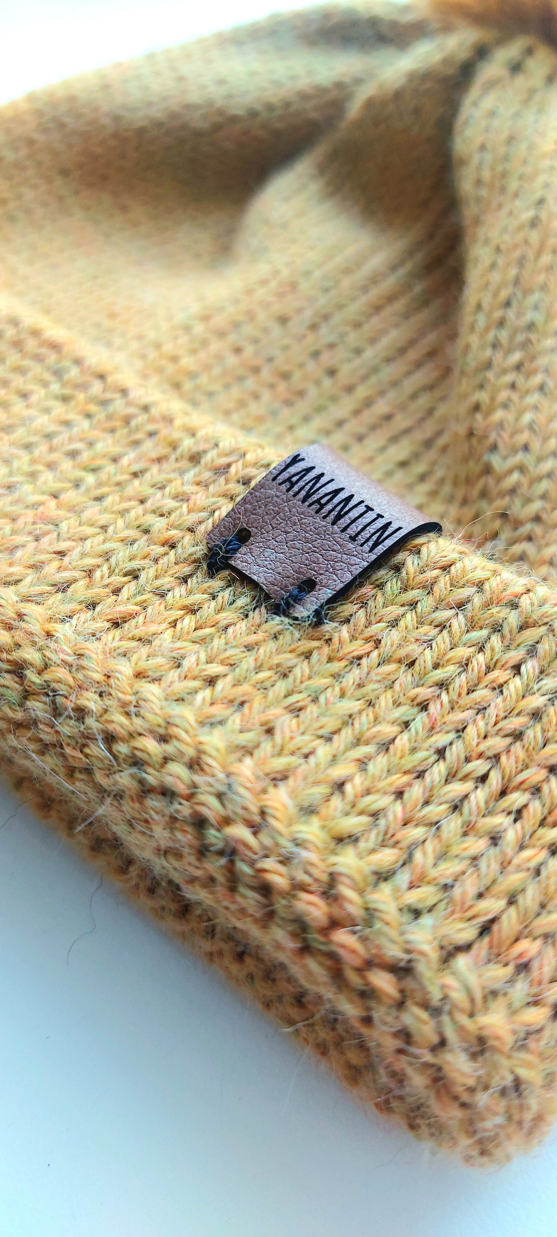 Close-up of the brown vegan leather label on the handmade light yellow baby hat, highlighting the quality and style.