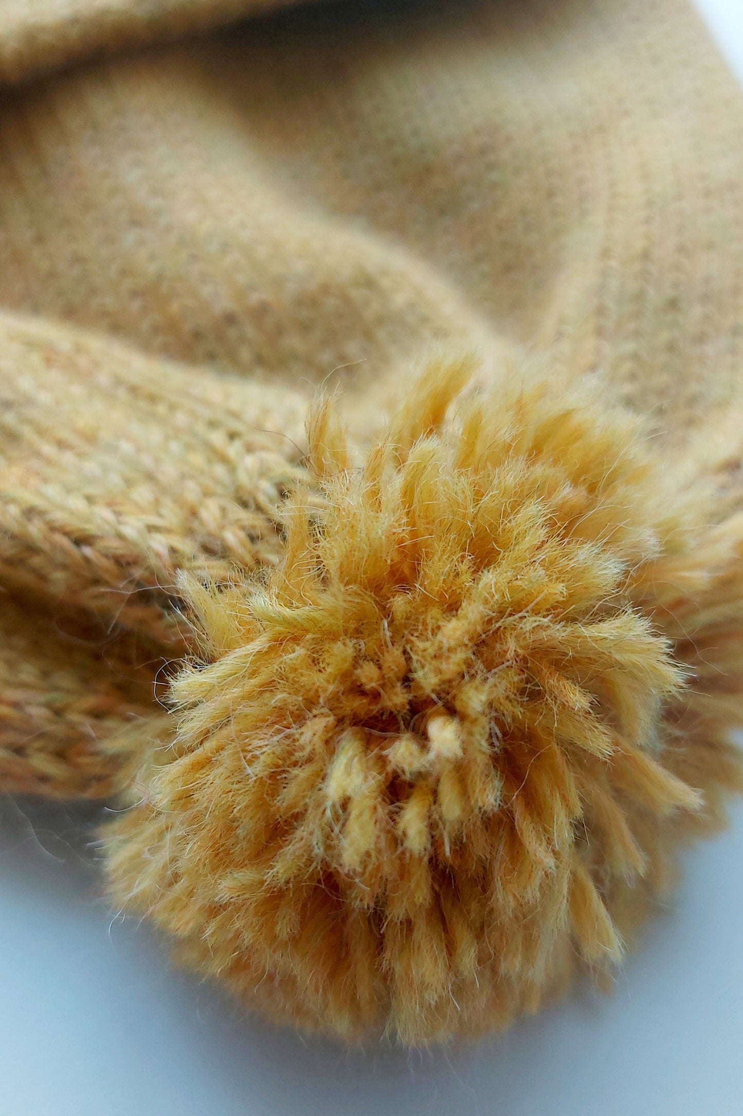 Close-up of the handmade light yellow baby hat’s pompom, made from soft 100% baby alpaca wool, with a foldable edge and brown vegan leather label.