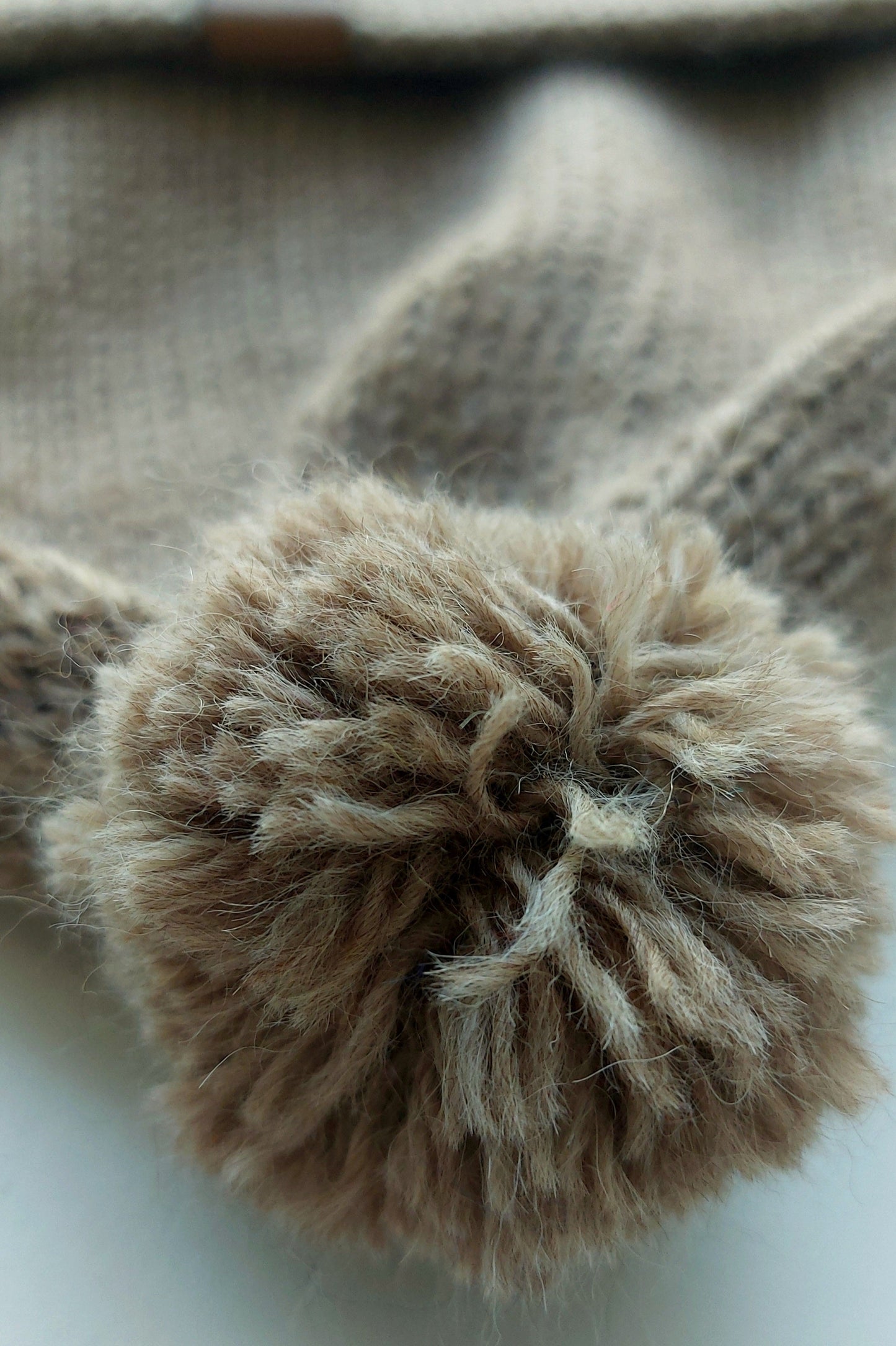 Close-up of the fluffy pompom on a light brown knitted baby hat, made from 100% baby alpaca wool.