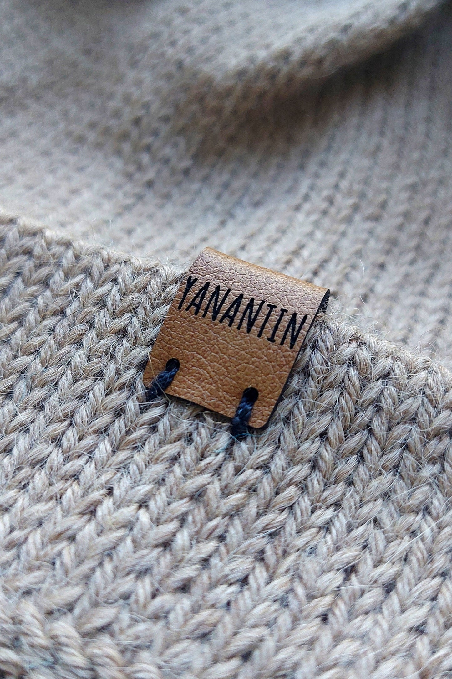 Close-up of the brown vegan leather label on a light brown knitted baby hat, made from 100% baby alpaca wool.