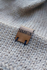 Close-up of the brown vegan leather label on a light brown knitted baby hat, made from 100% baby alpaca wool.