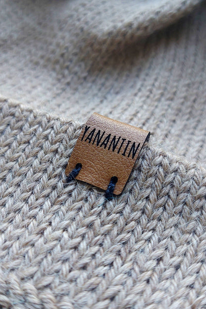 Close-up of the brown vegan leather label on a light brown knitted baby hat, made from 100% baby alpaca wool.