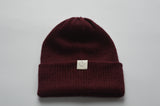Burgundy red knitted baby alpaca hat with a white organic cotton label and folded brim