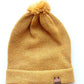 Handmade light yellow baby hat in soft 100% baby alpaca wool with a pompom, foldable edge, and brown vegan leather label, offering cozy warmth and cute design.
