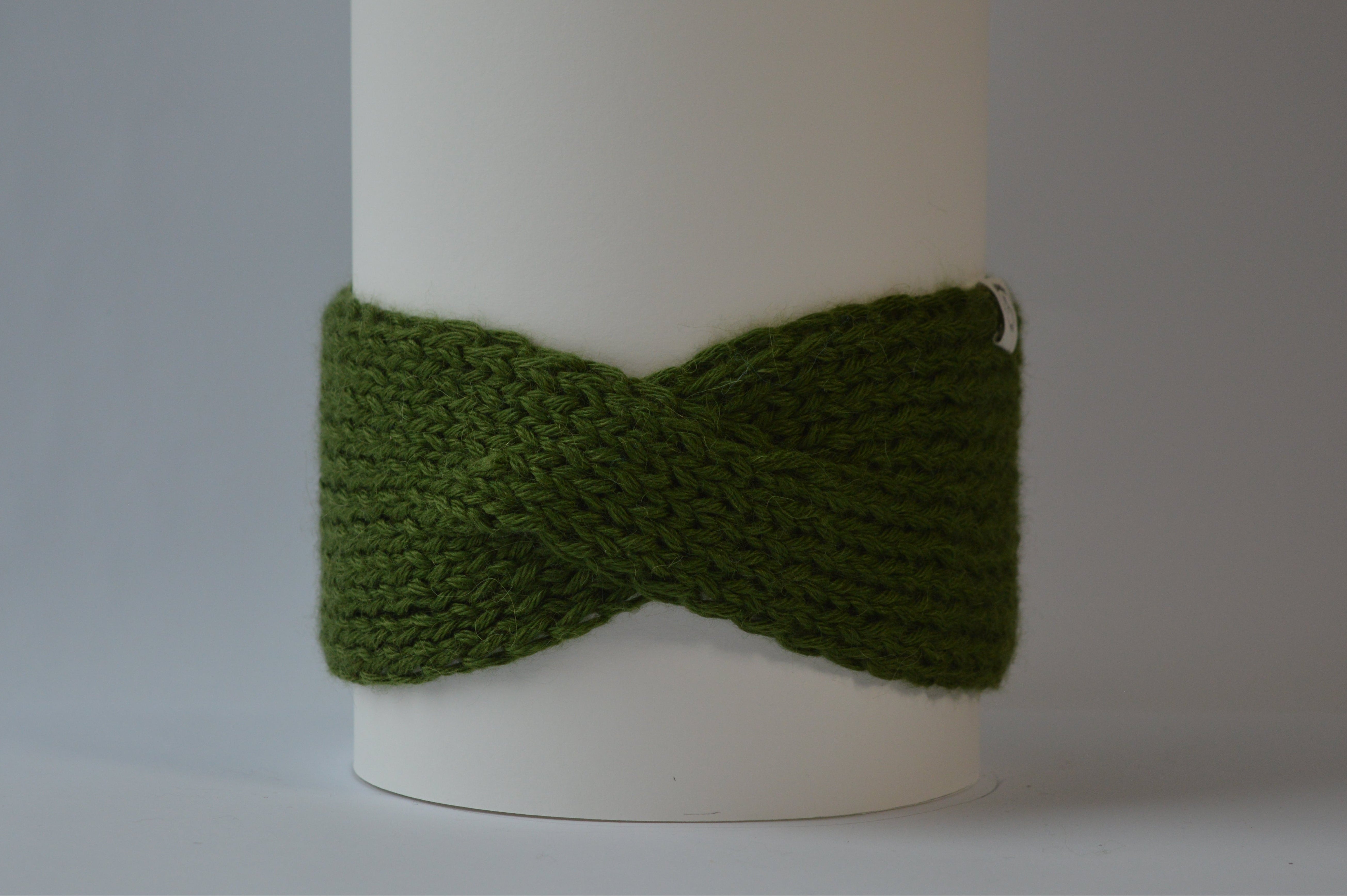 Chunky green knitted headband with a front twist against a gray background