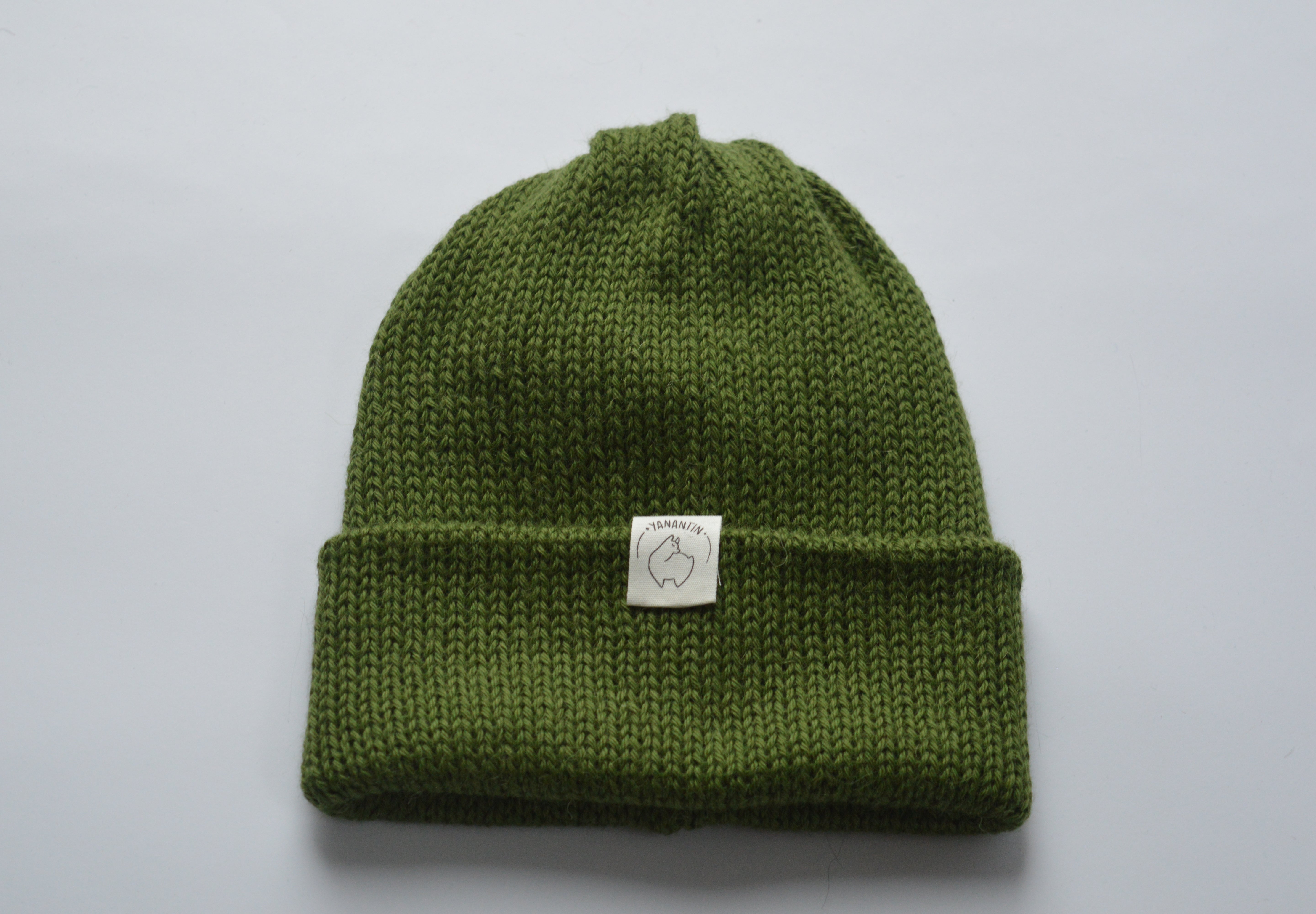 Moss green knitted baby alpaca hat with a white organic cotton label and folded brim