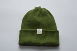Moss green knitted baby alpaca hat with a white organic cotton label and folded brim