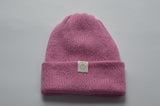 Pink knitted baby alpaca hat with a white organic cotton label and folded brim