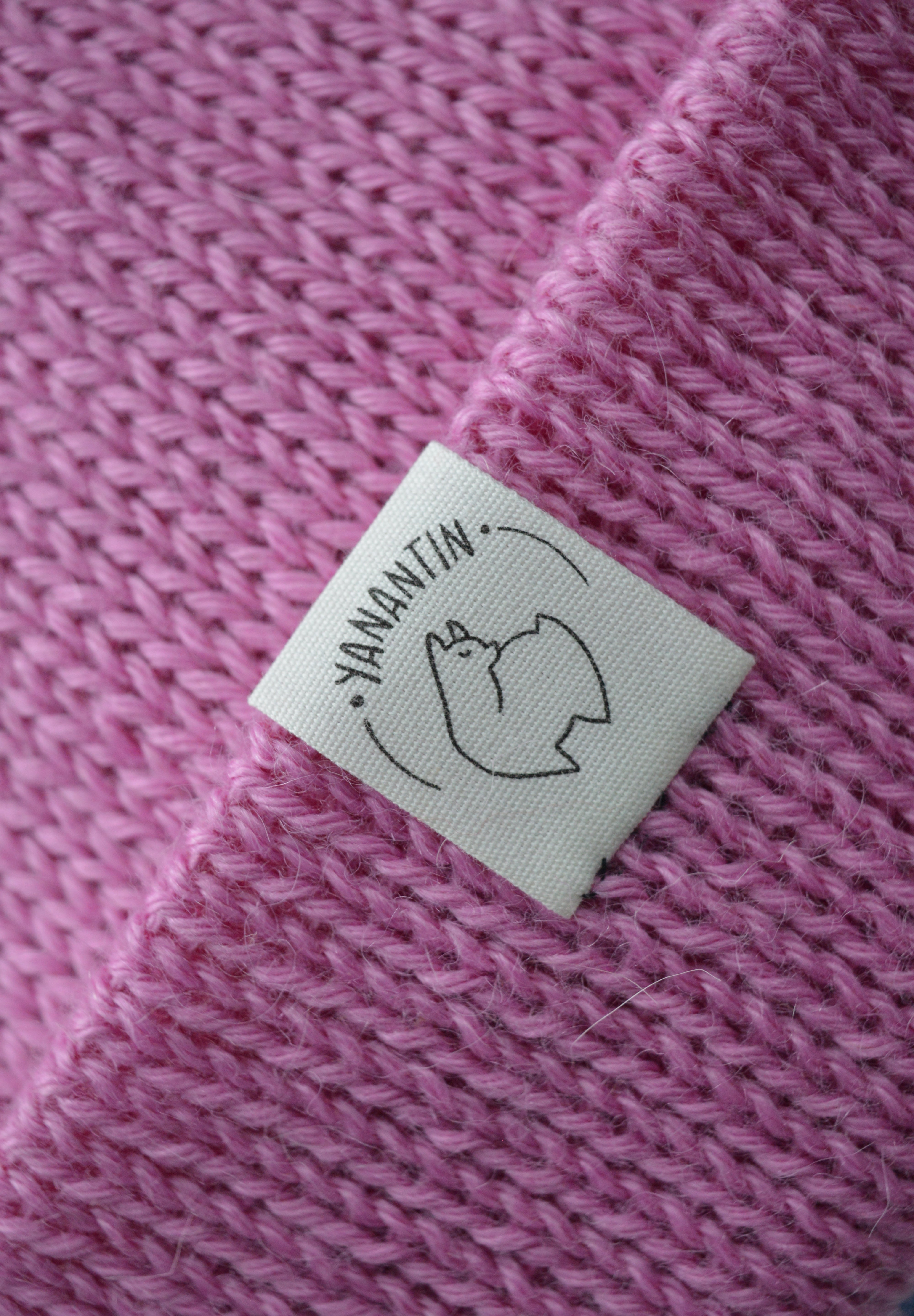 White organic cotton logo of a cute alpaca featuring the brand 'YANANTIN' on a pink woolen hat
