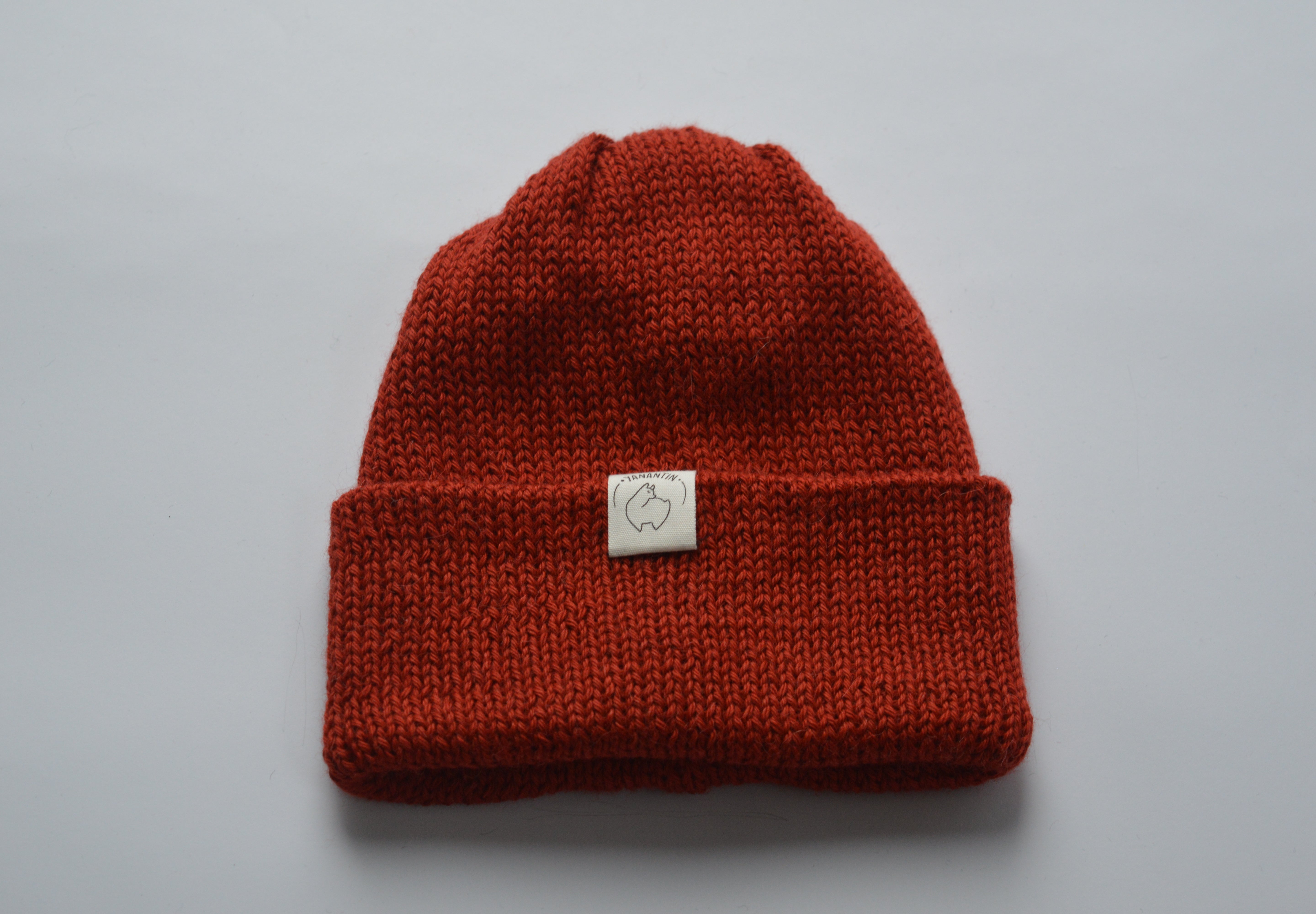 Deep orange knitted baby alpaca hat with a white organic cotton label and folded brim