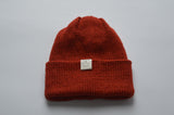 Deep orange knitted baby alpaca hat with a white organic cotton label and folded brim