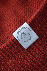 White organic cotton logo of a cute alpaca featuring the brand 'YANANTIN' on a red/orange woolen hat