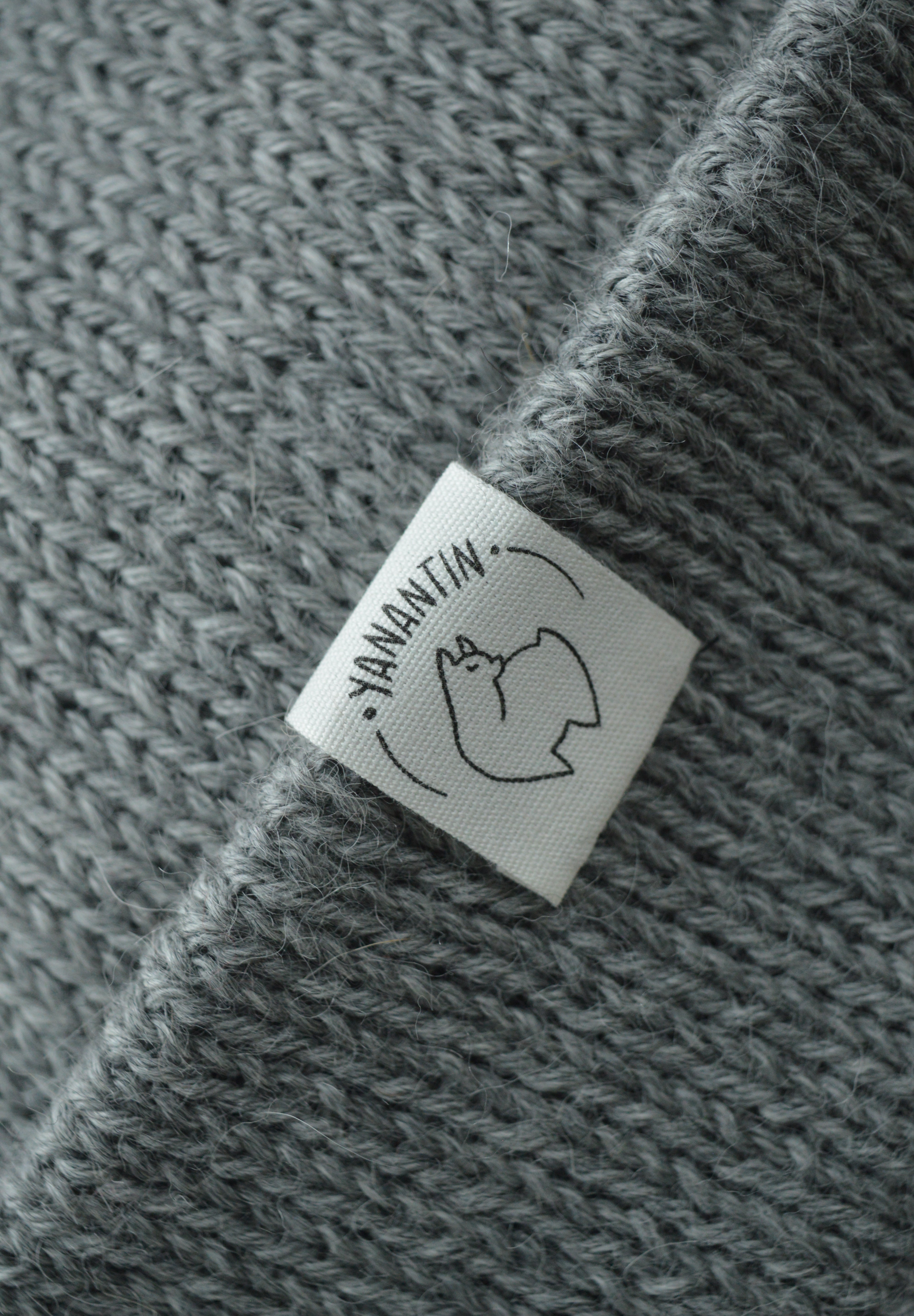 White organic cotton logo of a cute alpaca featuring the brand 'YANANTIN' on a light grey woolen hat