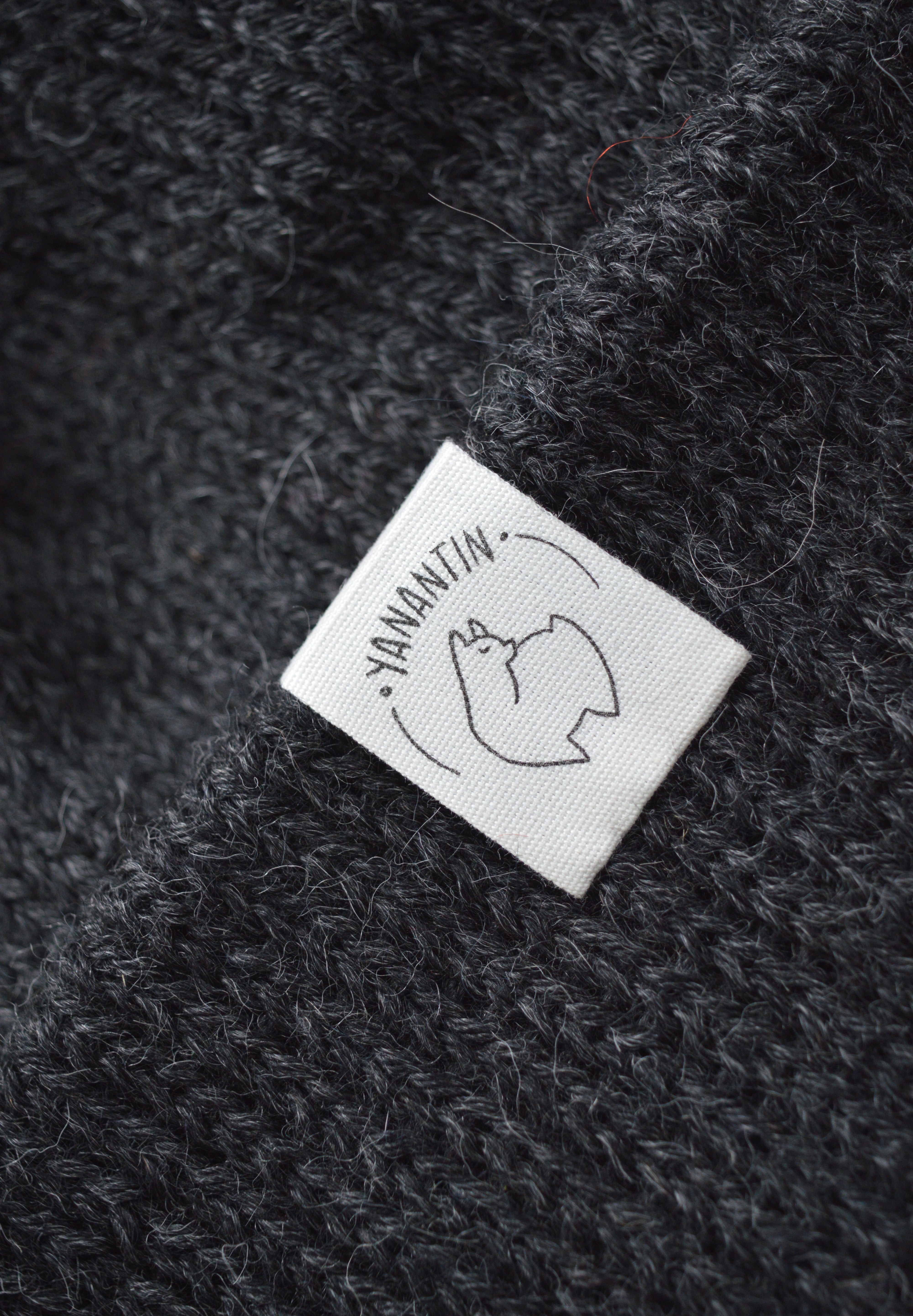 White organic cotton logo of a cute alpaca featuring the brand 'YANANTIN' on a  black woolen hat