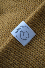Close-up of a label on a textured mustard yellow knitted hat  of the brand 'YANANTIN'