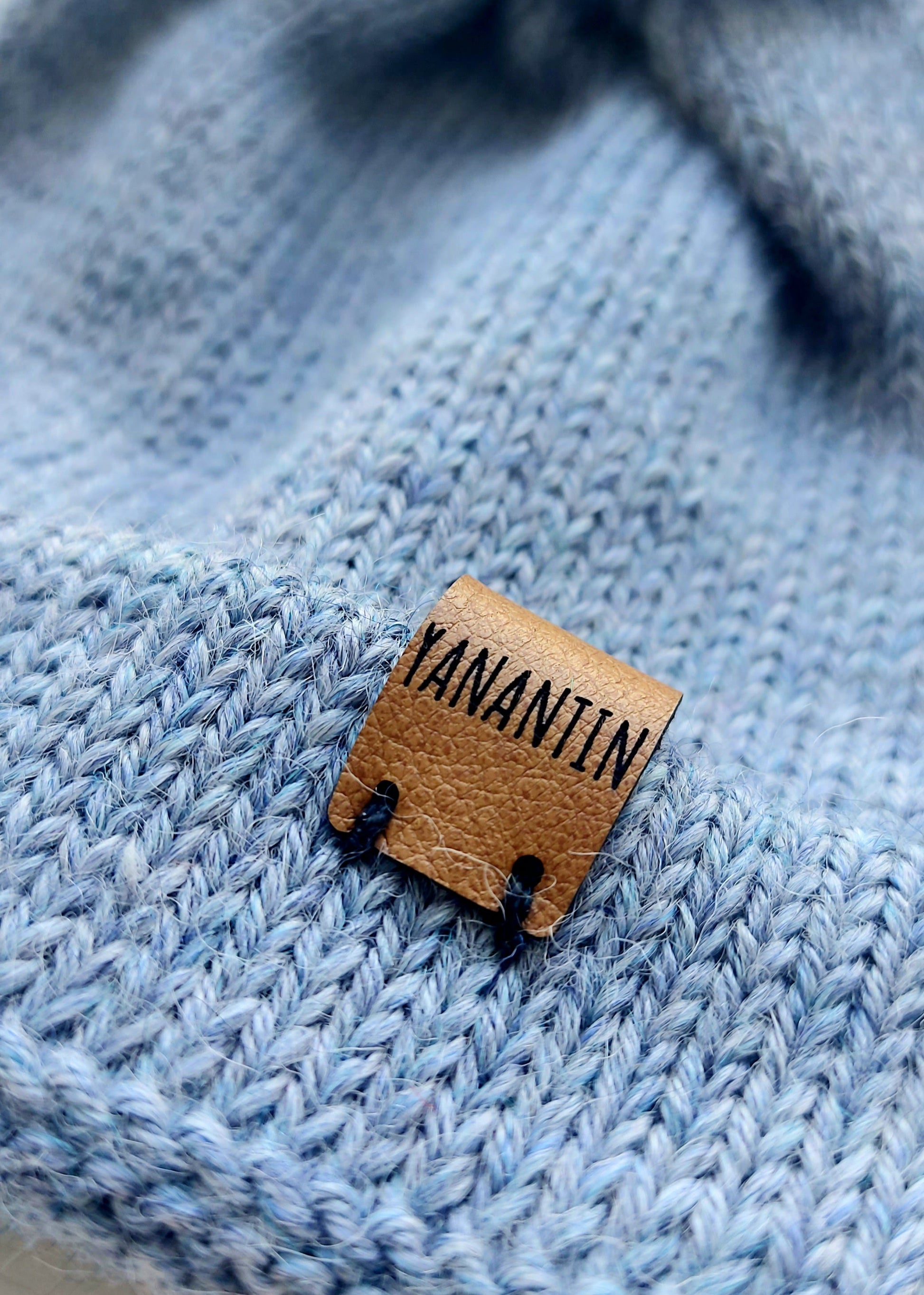 Close-up of the brown vegan leather label on the handmade light blue baby hat, highlighting its quality and style.