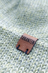 Close-up of the brown vegan leather label on the handmade light green baby hat, highlighting its quality and style.