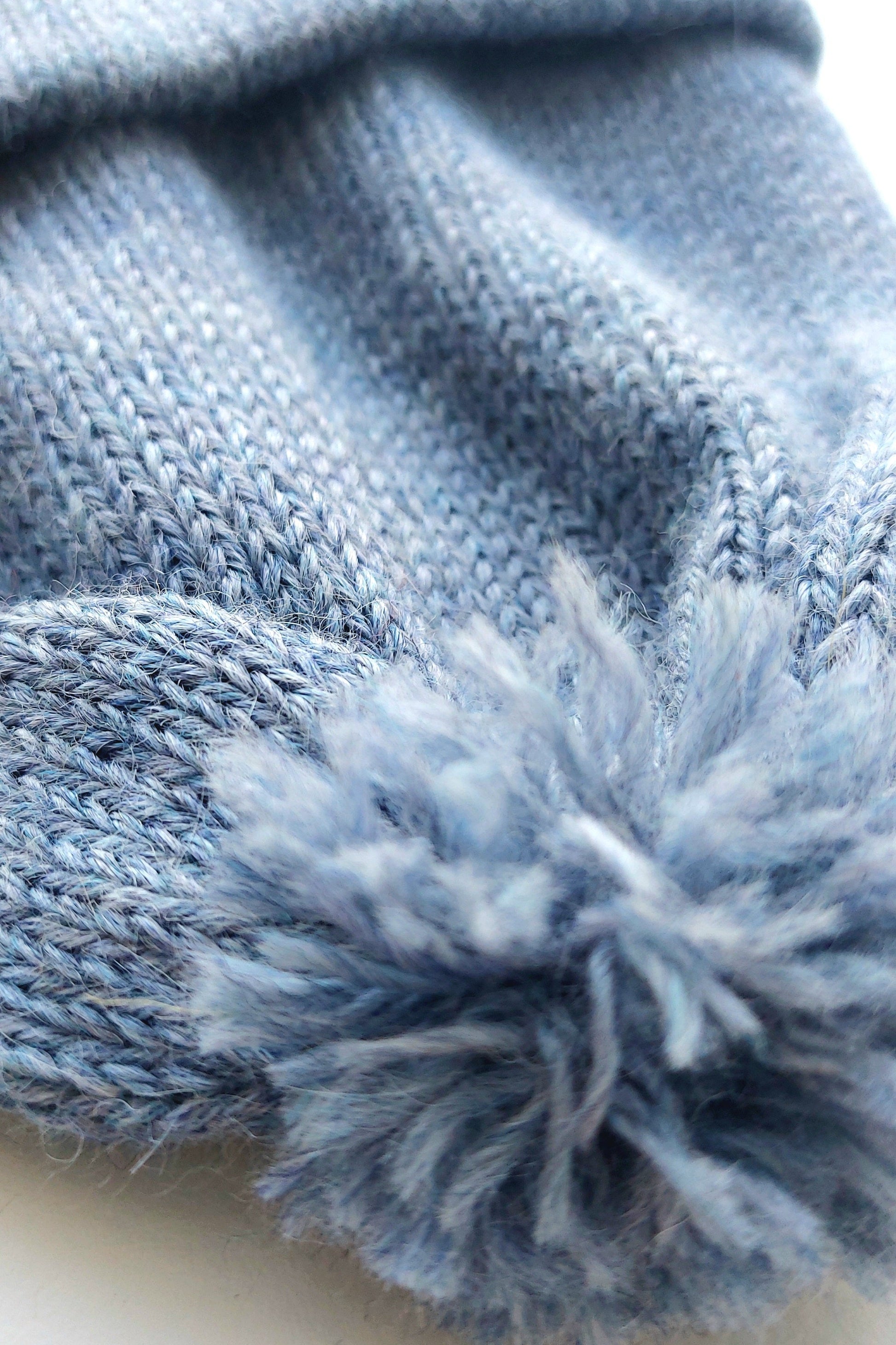 Close-up of the pompom on the handmade light blue baby hat, made from soft 100% baby alpaca wool with a foldable edge and brown vegan leather label.