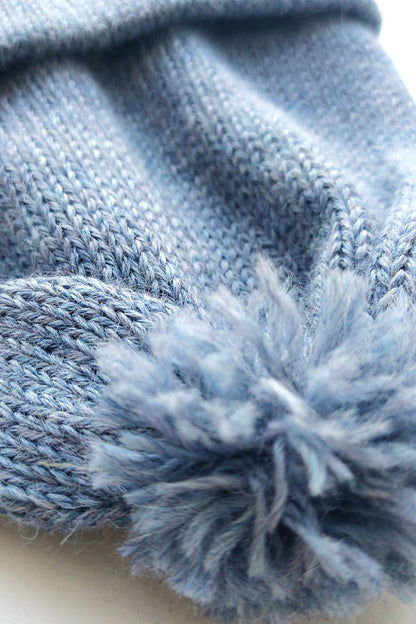Close-up of the pompom on the handmade light blue baby hat, made from soft 100% baby alpaca wool with a foldable edge and brown vegan leather label.