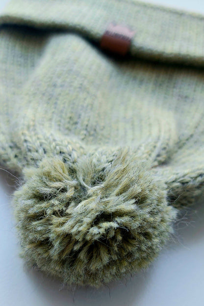 Close-up of the pompom on the handmade light green baby hat, made from soft 100% baby alpaca wool with a foldable edge and brown vegan leather label.