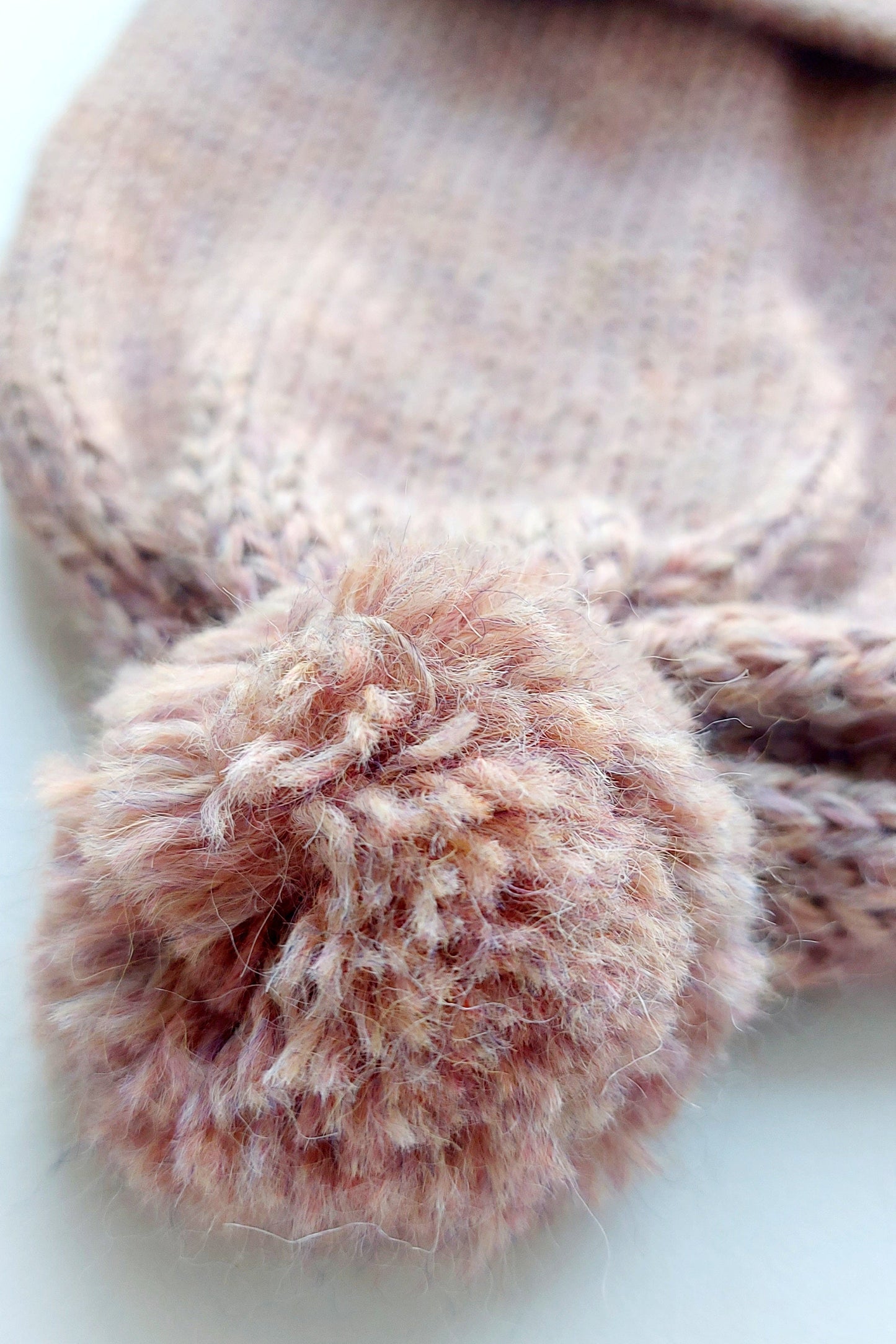Close-up of the pompom on the handmade light pink baby hat, made from soft 100% baby alpaca wool with a foldable edge and brown vegan leather label.