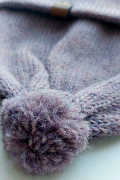 Close-up of the pompom on the handmade lila baby hat, made from soft 100% baby alpaca wool with a foldable edge and brown vegan leather label.