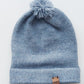 Handmade light blue baby hat in soft 100% baby alpaca wool with a pompom, foldable edge, and brown vegan leather label, offering warmth and comfort.