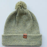 Handmade light green baby hat in soft 100% baby alpaca wool with a pompom, foldable edge, and brown vegan leather label, offering warmth and style.
