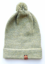 Handmade light green baby hat in soft 100% baby alpaca wool with a pompom, foldable edge, and brown vegan leather label, offering warmth and style.
