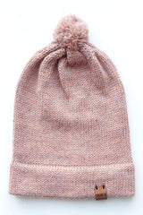 Handmade light pink baby hat in soft 100% baby alpaca wool with a pompom, foldable edge, and brown vegan leather label, offering warmth and comfort.