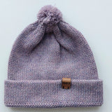 Handmade lila baby hat in soft 100% baby alpaca wool with a pompom, foldable edge, and brown vegan leather label, offering warmth and comfort.