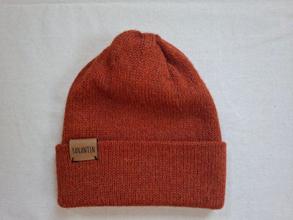 Orange alpaca wool knit beanie with a visible brand label on a light gray background