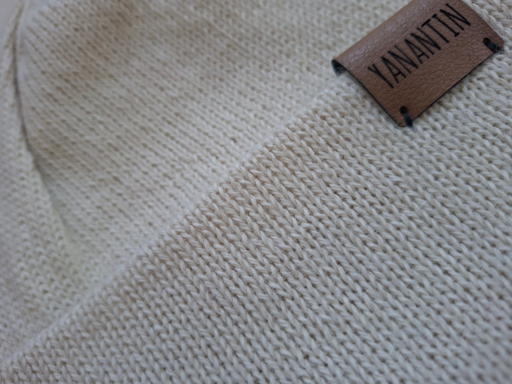 Close-up of a beige knitted wool fabric with a 'YANANTIN' label on a textured background