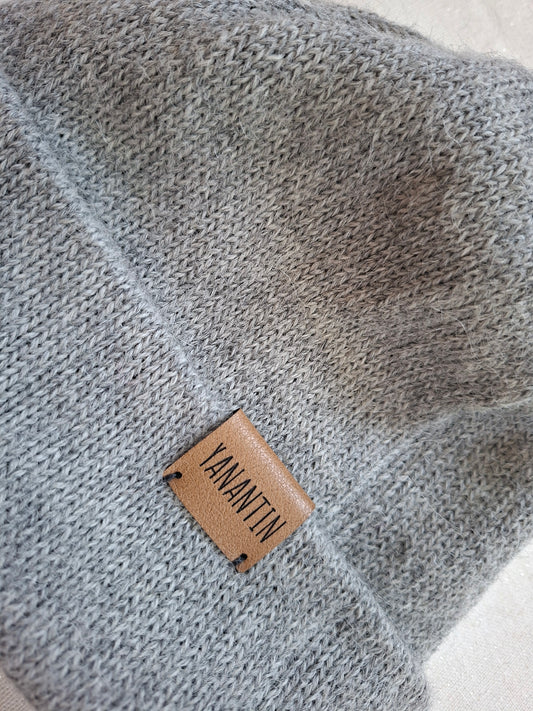 Close up of a gray knitted wool hat with a brown leather label displaying 'YANANTIN'.