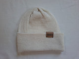 Beige knit beanie with a brown leather patch on a light gray background