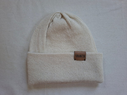 Beige knit beanie with a brown leather patch on a light gray background
