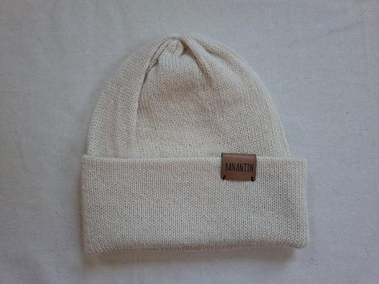 Beige knit beanie with a brown leather patch on a light gray background
