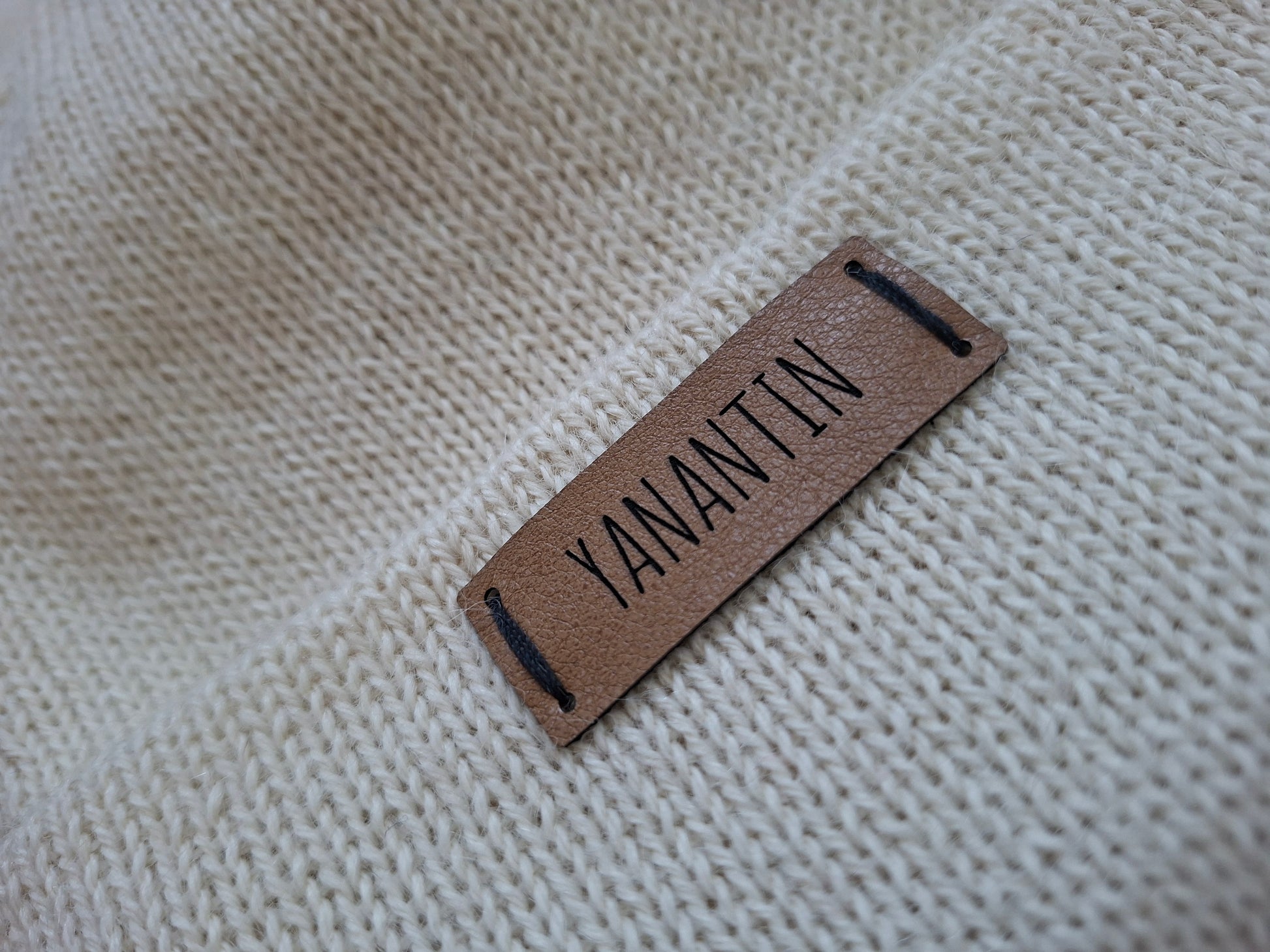 Brown vegan leather label with 'YANANTIN' text on a beige knitted wool fabric background